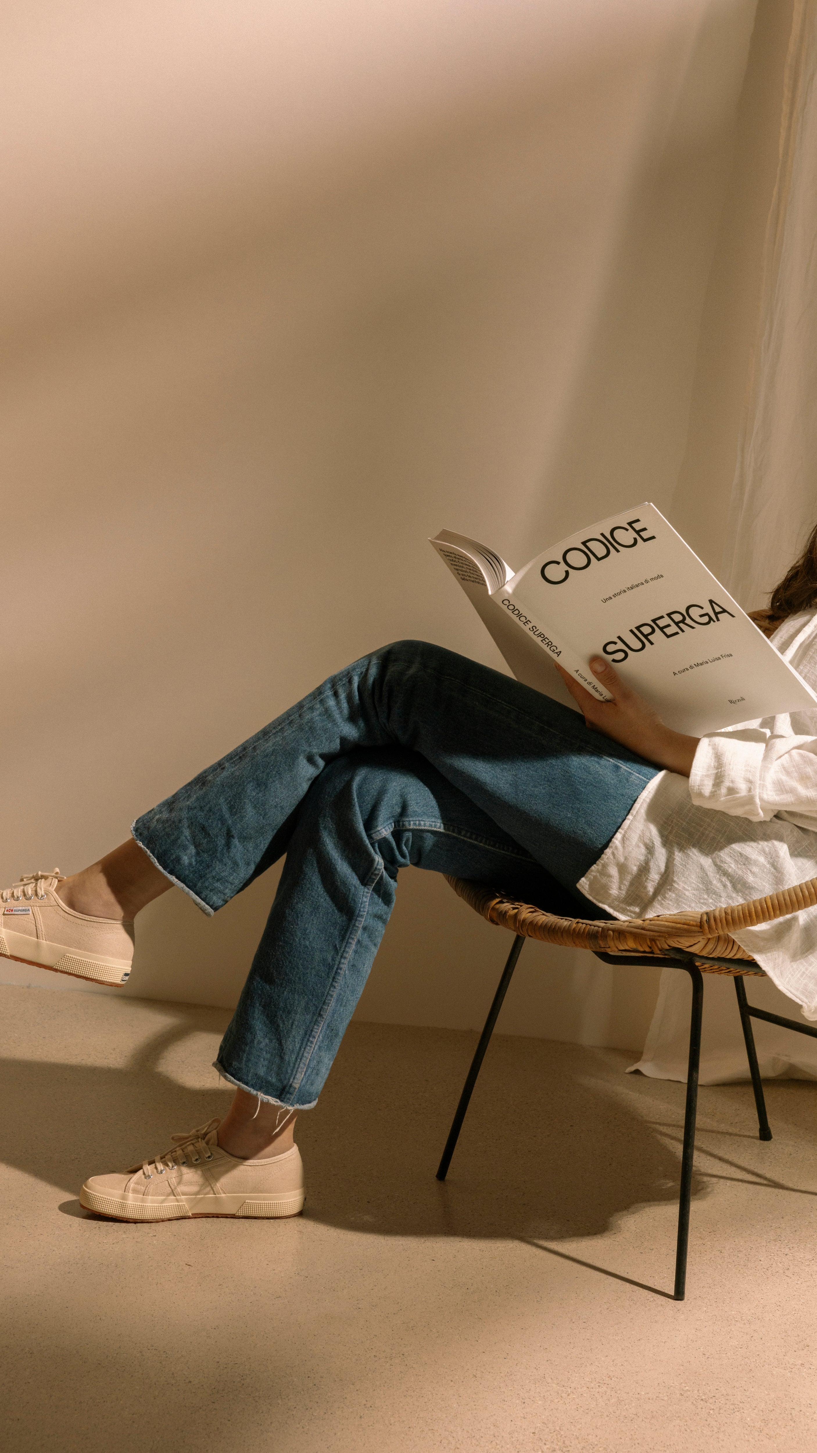 Person sitting on a chair holding a 'Superga' newspaper against a beige wall.