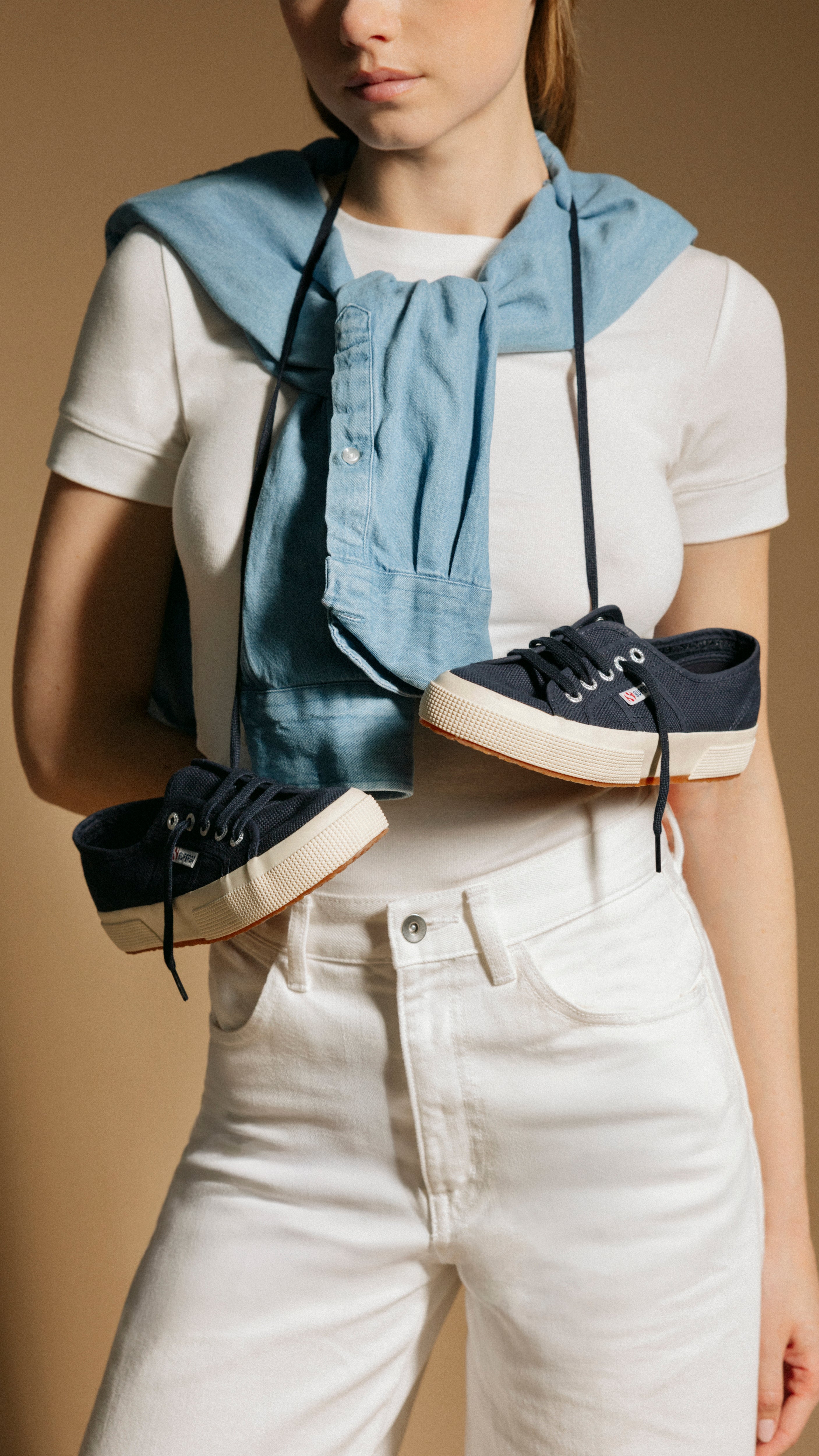 Person holding navy sneakers with white soles against a beige background