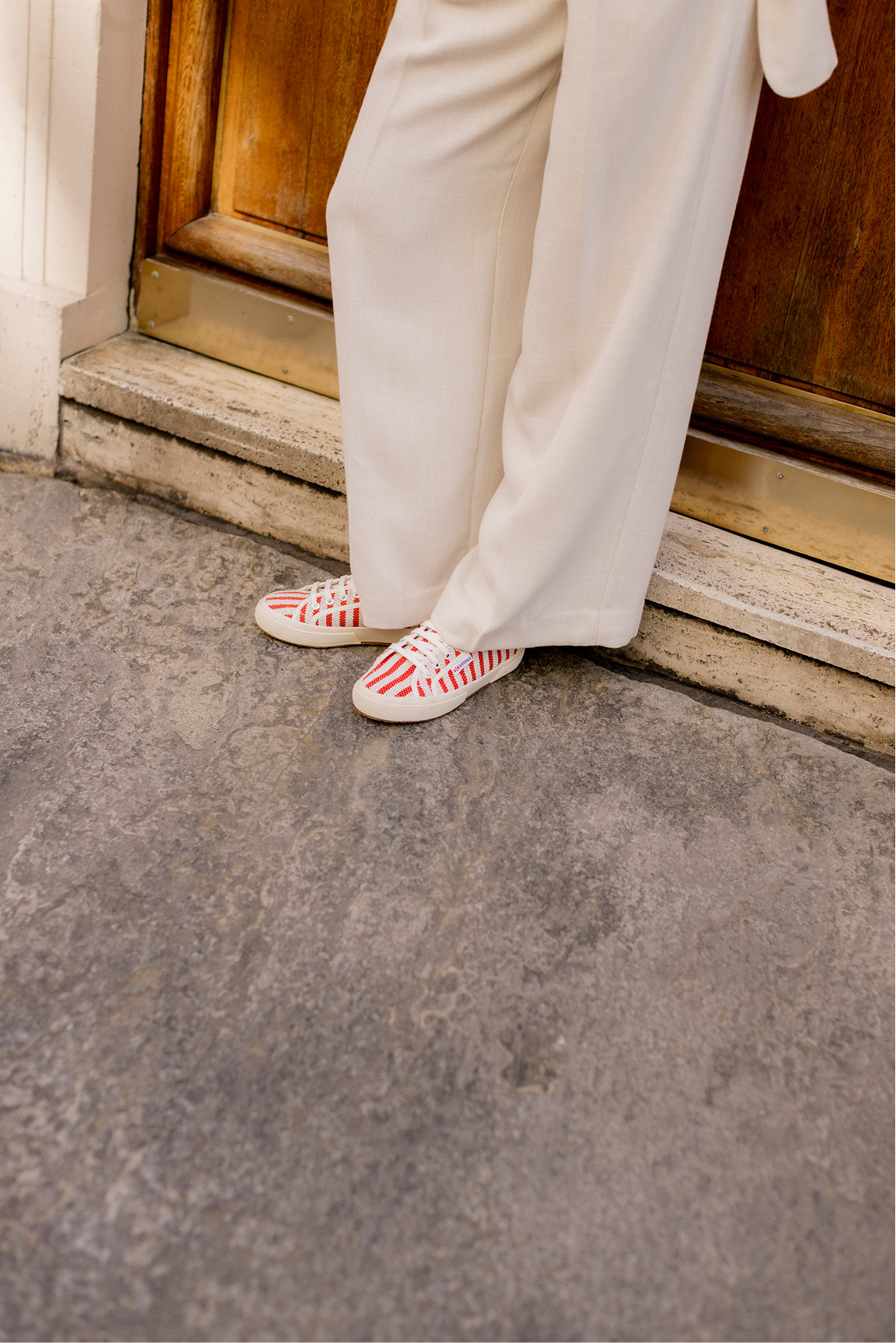 Person wearing white pants and red and white sneakers stepping onto a concrete surface.